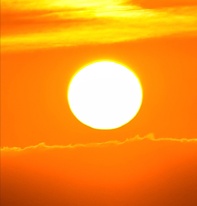 The sun glowing yellow-white hot in an orange sky.